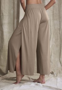 Beige wide-leg pants with an elastic waistband, featuring side slits. Smooth, lightweight fabric, and a relaxed fit.