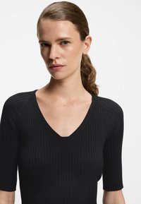 Schwarzes, geripptes Strickoberteil mit tiefem V-Ausschnitt und kurzen Ärmeln, das eine figurbetonte Silhouette mit einem strukturierten Muster zeigt.