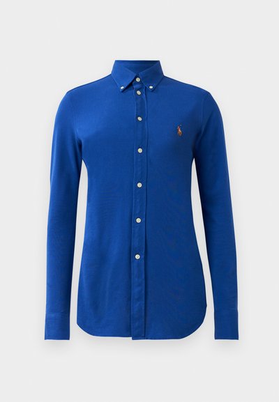 Camisa azul de manga longa abotoada, feita de algodão, com um colarinho clássico, botões brancos e um pequeno logótipo bordado no lado esquerdo do peito.