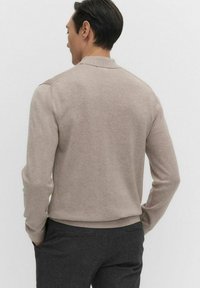 Vaaleanbeige neulepaita, jossa on pitkät hihat ja kaulus. Paita on sileäpintainen ja ribbaushelma, kuvattu takaa valkoista taustaa vasten.