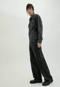 Casaco de ganga preto com dois bolsos no peito, combinado com jeans pretos de corte largo e calçado preto. Textura suave e detalhes mínimos.