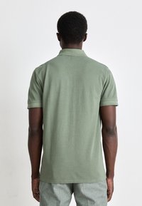 Grønn polo skjorte med krage og korte ermer, laget av myk bomull. Har et rent bakdesign uten synlige logoer eller detaljer.