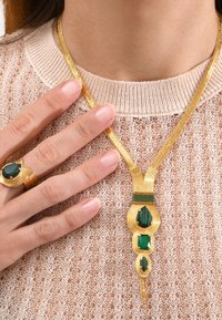 Pendentif en or avec des pierres précieuses vertes, présentant un design complexe en forme de vagues et une chaîne. Accompagné d'une bague en or assortie.