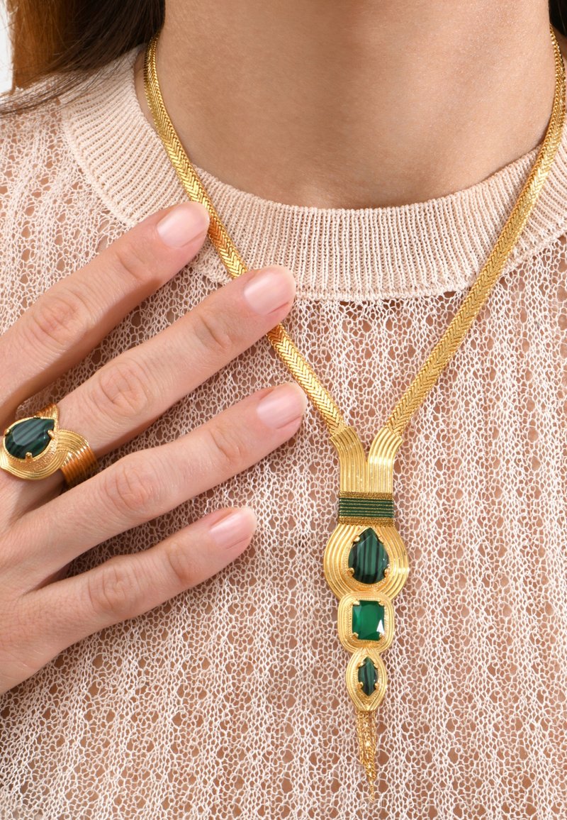 Pendentif en or avec des pierres précieuses vertes, présentant un design complexe en forme de vagues et une chaîne. Accompagné d'une bague en or assortie.