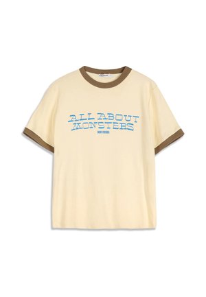 Camiseta beige de manga corta con ribete marrón en el cuello y las mangas, con texto azul "ALL ABOUT MONSTERS" en el frente.