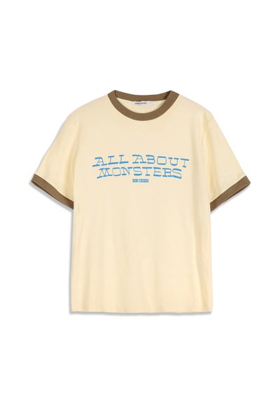 T-shirt beige à manches courtes avec bordure marron au col et aux manches, avec un texte bleu "ALL ABOUT MONSTERS" sur le devant.
