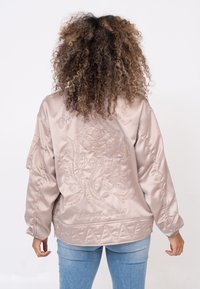 Giacca bomber in satin rosa chiaro con ricami floreali sulla schiena, dotata di orlo trapuntato e polsini elasticizzati.