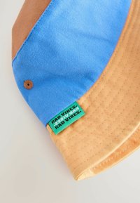 Bucket-Hut mit blauer Krone und beigem Schirm, aus strukturiertem Stoff gefertigt. Mit einem grünen Etikett, auf dem "RAD VIBES" gestickt ist.