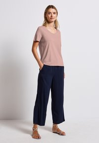 Světle růžové tričko s krátkým rukávem a kulatým výstřihem, kombinováno s tmavě modrými širokými nohavicemi a stříbrnými sandály na pásku.