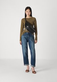 Zwarte leren schoudertas, olijfgroene langarmshirt, blauwe straight-leg jeans met opgerolde manchetten, en bruine versierde sandalen.