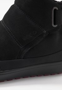 Botte de cheville ECCO noire avec semelle texturée, tige en cuir cousue et détail en tissu sur le côté.