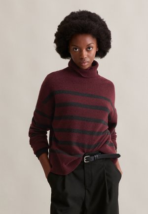Maglione a collo alto bordeaux con strisce orizzontali nere, texture a maglia, spalle scese e vestibilità rilassata, abbinato a pantaloni scuri e una cintura.