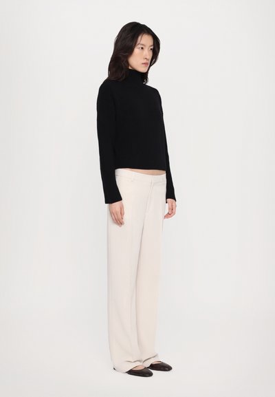 Black cropped turtleneck sweater with ribbed texture, paired with high-waisted, wide-leg cream trousers and flat black shoes.