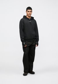 Camisola preta com capuz e bolso frontal, combinada com calças largas escuras e luvas. Textura suave, design minimalista e um logótipo simples no capuz.