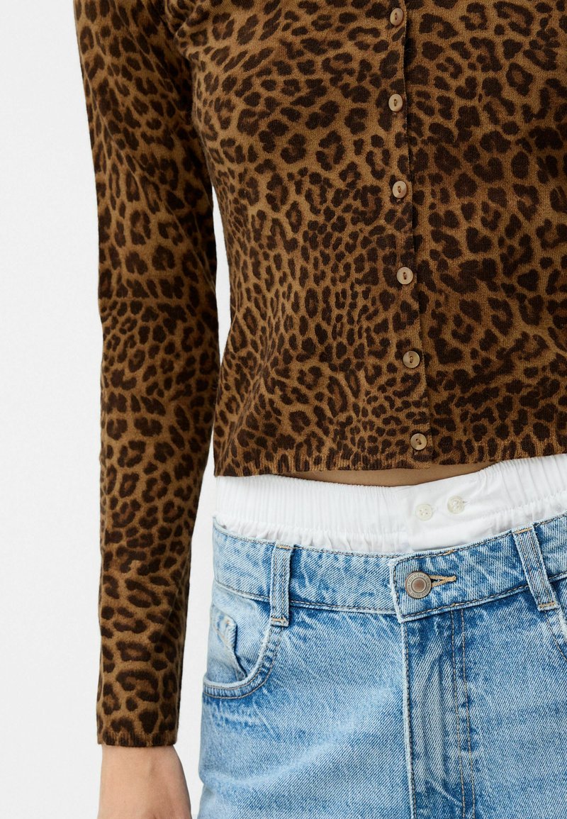 Braun Leoparddruck-Cardigan mit Rundhalsausschnitt, Knopfverschluss und langen Ärmeln; kombiniert mit hellblauen hochgeschnittenen Jeans.