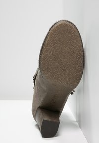 Bottine en daim gris avec un talon bloc, semelle en caoutchouc texturée et détails latéraux avec un design à franges.