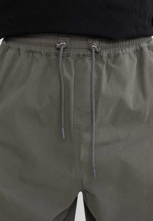 Khakifarbene Shorts mit Kordelzug, elastischem Bund, strukturiertem Gewebe und grauen Kordelakzenten. Keine sichtbaren Taschen in der Frontalansicht.