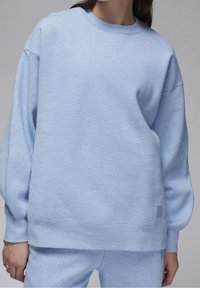 Sudadera XXL de color azul claro, hecha de un material suave, con hombros caídos, puños acanalados y una pequeña etiqueta con el logo en el dobladillo.