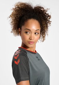 Kortärmad sporttröja i grått tyg med en slät textur, med röda detaljer och geometriska mönster på axlarna.