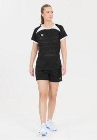 Svart sportt-shirt med vita detaljer och logotyp, ihop med svarta shorts. Tyget är lätt och strukturerat, utformat för atletisk användning.