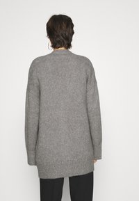 Grå stickad tröja med avslappnad passform, ribbade ärmslut och nederkant. Bakdelen har en hög-låg-design med en texturerad yta.