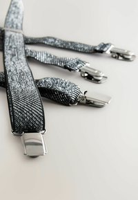 Svarta och silverfärgade strukturerade hängslen med metallklämmor liggande platt på en ljus bakgrund.