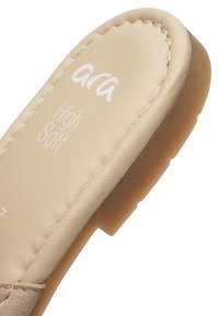 Beige polstret skosål med hvid syning og "Ara High Soft" trykt på overfladen, med en lys brun fleksibel sål.