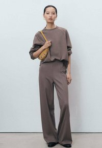 Bruine oversized sweatshirt en bijpassende wijde broek gemaakt van zachte stof. Voorzien van een kleine gele tas met decoratieve hardware.