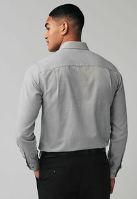 Camisa gris de manga larga con un patrón texturizado sutil, puños abotonados y cuello clásico, combinada con pantalones negros.