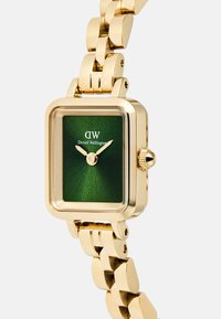Gold square watch with green dial, minimal gold hands, "DW Daniel Wellington" logo, and matching gold linked bracelet band.