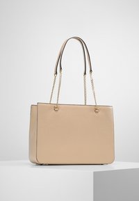 Nákupní taška v světlé béžové barvě s texturovaným povrchem, s dvojitými řetízkami a kontrastním černým lemem podél okrajů.