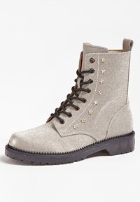 Botte de combat lacée gris clair avec semelle noire et petites clous en forme d'étoile dorée sur le côté, dotée d'une languette à l'arrière.