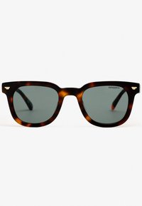 Gafas de sol carey con lentes verdes, forma cuadrada y cejas pronunciadas. Acentos dorados en el marco y logo de la marca visible.