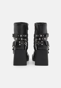 Black heeled ankle boots with a glossy finish, featuring studded straps, zippers, and a square block heel for stability.