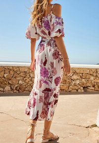 Robe maxi florale blanche avec des motifs violets et rouges, dotée de manches ballons, d'un corsage ajusté et d'une jupe à volants. Sandales à lanières.