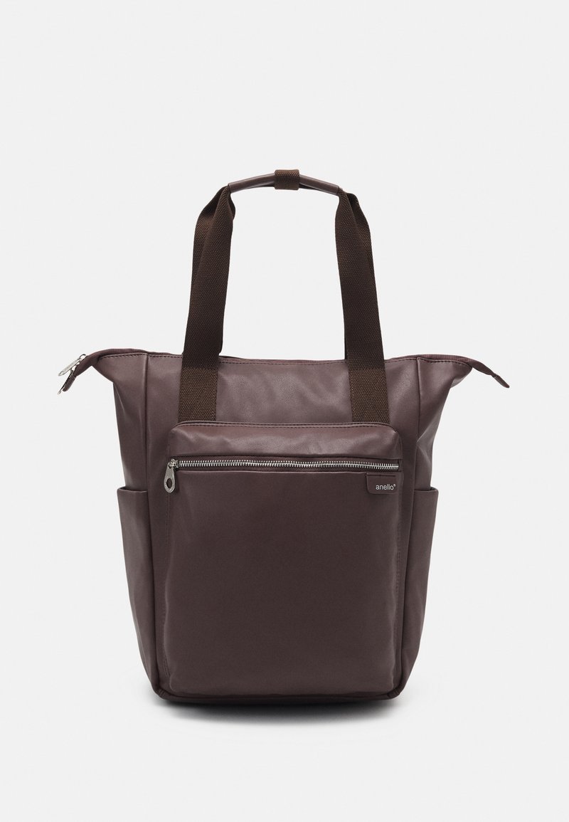 Sac cabas marron avec deux poignées en tissu foncé, poche avant zippée, poches latérales et fermeture éclair au sommet, présenté sur fond blanc.