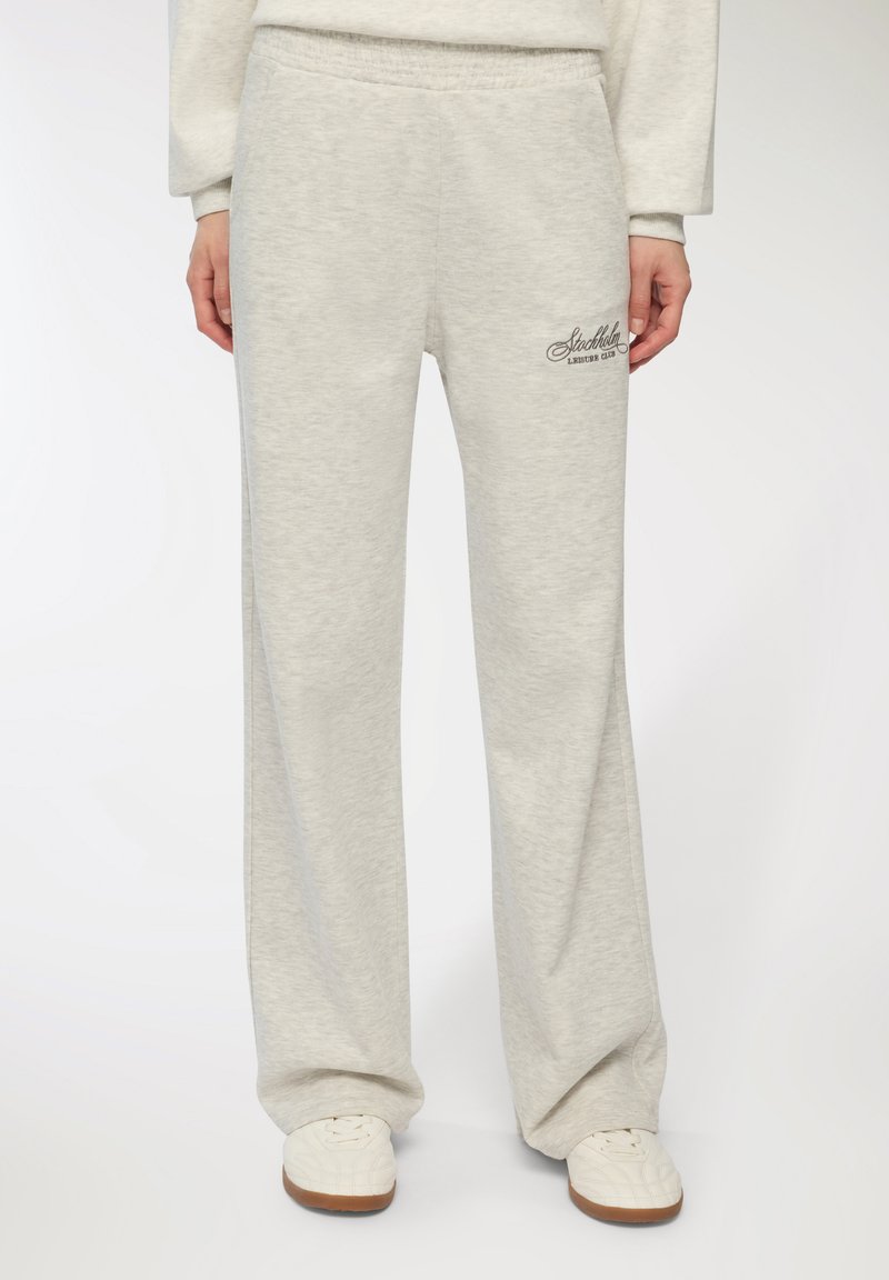 Jasnoszare dresy z miękkiego materiału, z szerokimi nogawkami, elastycznym paskiem w talii i haftowanym logo na lewym biodrze.