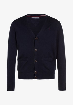 Cárdigan azul marino con cuello en V, cinco botones marrones, dos bolsillos delanteros y un pequeño logo rojo, blanco y azul en el pecho izquierdo.