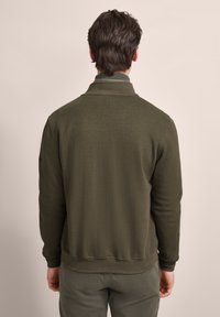 Olive green sweatshirt with a high collar, ribbed cuffs, and a smooth texture. Features a logo on the left sleeve and a relaxed fit.