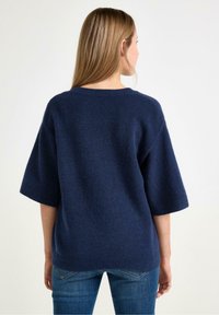 Granatowy, oversize'owy sweter wykonany z teksturowanej tkaniny, z krótkimi rękawami i okrągłym dekoltem, w połączeniu z jasnoniebieskimi dżinsami.