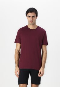 Burgundi crew neck póló, pamutból készült, rövid ujjú, mellkason kis logóval. Fekete rövidnadrággal párosítva.