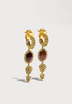 Boucles d'oreilles créoles dorées avec pierres ovales rouge foncé et grappes de perles suspendues sur un fond clair.