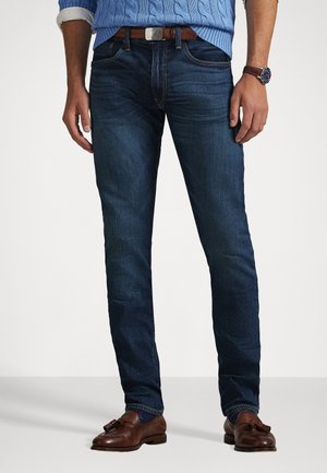 Dunkelblaue Denim-Jeans mit Slim-Fit, featuring dezente Used-Optik, Fünf-Taschen-Design und einem braunen Ledergürtel mit einer Metall-Schnalle.