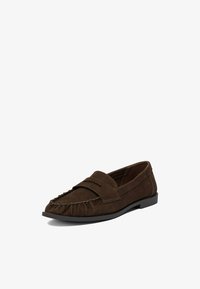 Mocasín de ante marrón oscuro con punta mocasín cosida y suela plana negra, visto en un ligero ángulo sobre un fondo blanco.