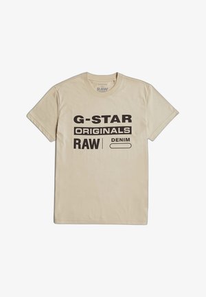 T-shirt beige en coton avec un texte noir audacieux : "G-STAR RAW ORIGINALS DENIM." Col rond classique et manches courtes. Texture du tissu uni.