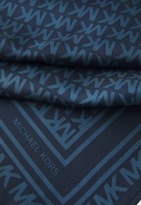 Tessuto blu a motivo con logo "MK" ripetuto in blu scuro, con una texture liscia e una leggera lucentezza. Stampato "MICHAEL KORS".