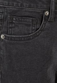 Jeans en denim noir avec une finition texturée, un design à cinq poches et des éléments en métal sur la taille et la poche.