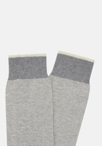 Pelēkas un gaiši pelēkas svītrainas zeķes ar vienkrāsainu pelēku maliņu. Tekstūra izskatās gluda, ar ribotu malas augšdaļu. Akcenti gaišākā krāsā pie maliņas.