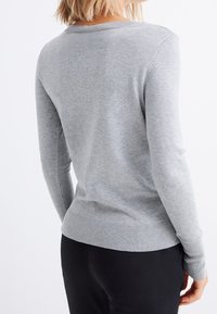 Grauer Strickpullover mit langen Ärmeln, gerippten Bündchen und Saum, glatter Textur, figurbetontem Design. Keine sichtbaren Muster oder Verzierungen.