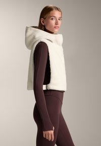 Crème, gestructureerde fleece vest met een capuchon, cropped ontwerp en verstelbare zijgesp. Gedragen over een fitted donkerbruin top.